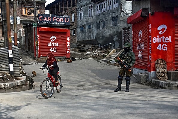 gettyimages : A girl rides a bicycle as policeman stands guard during curfew in Srinagar |
